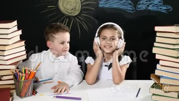 回到学校的概念。 男孩和女孩坐在书桌前，桌上放着一大堆书，黑板后面放着孩子们的图画