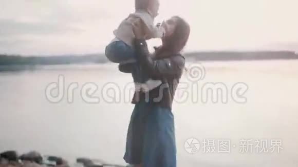母亲牵着儿子的手在海滩的岸边。 微笑的女人抱起她的小男孩，亲吻拥抱