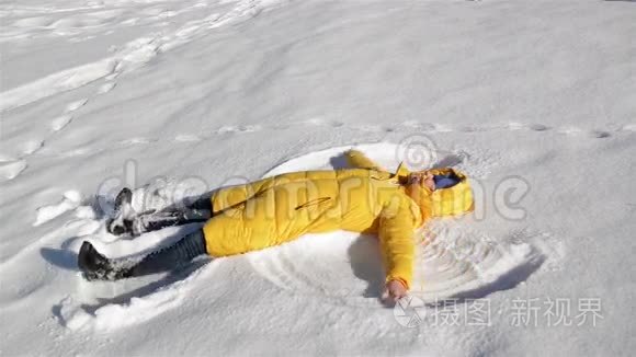 快乐的年轻女人躺在地上，做雪天使。 在干净的白色表面上穿黄色夹克的女孩