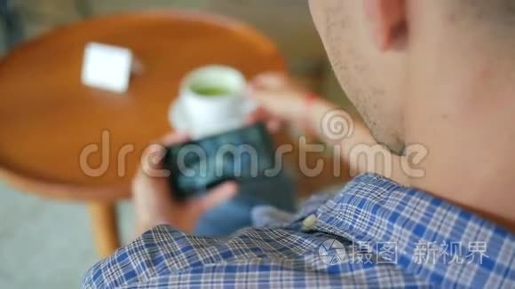 年轻英俊的男人在咖啡厅喝抹茶，在手机上看视频。 HD慢动作生活方式