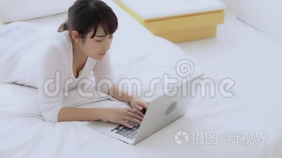 美丽的亚洲年轻女子躺在床上，在卧室里用手提电脑上网购物