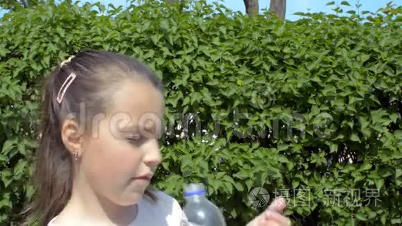 一个女孩在绿色灌木丛中喝塑料瓶里的水。