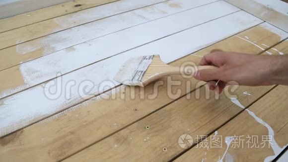 工人`手握毛笔，在木露台，天然木地板或墙面纹理表面涂刷白色..