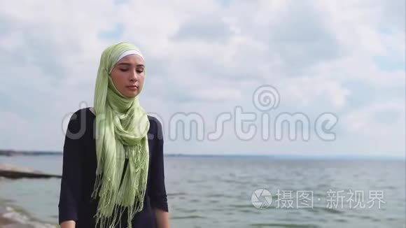 一位戴着面纱的年轻穆斯林妇女带着沉思的目光沿着大海走来