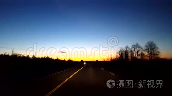 在日出期间驾驶乡村公路。 太阳清晨在地平线上升起时的驾驶视角