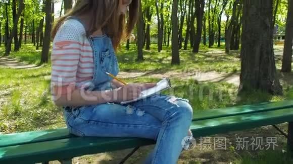 一个十几岁的女孩汲取自然。 一个戴手镯的女孩在公园里画画。 少年的手。
