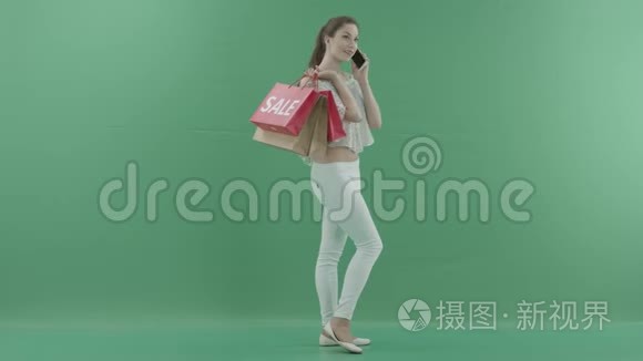 漂亮的年轻女子带着袋子在智能手机上谈论绿色屏幕