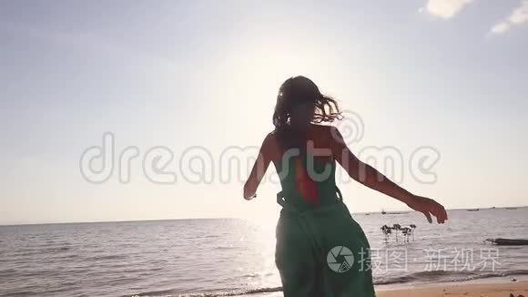 穿着绿色衣服在海滩上奔跑的漂亮年轻女子，慢悠悠地旋转着，举起双臂享受自由