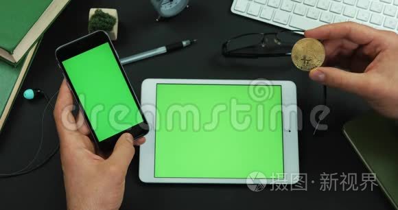 男人拿着一台绿色屏幕平板电脑和一台比特币的智能手机