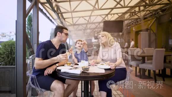 男孩和父母坐在一起，在自助餐厅的露台上用餐