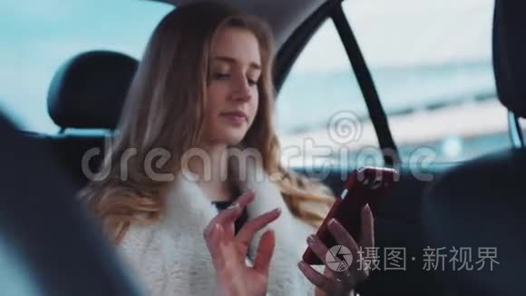 一位漂亮的年轻女士，她的蓝眼睛和一头金发，在开车进来的时候用手机应用程序给她的朋友发信息