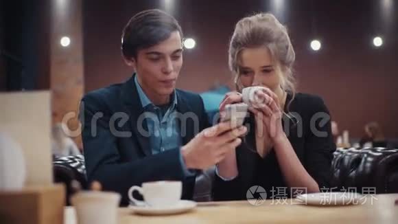 一对年轻夫妇在©咖啡馆约会。 一个手里拿着智能手机的男人和一个正在喝咖啡的女孩很活泼