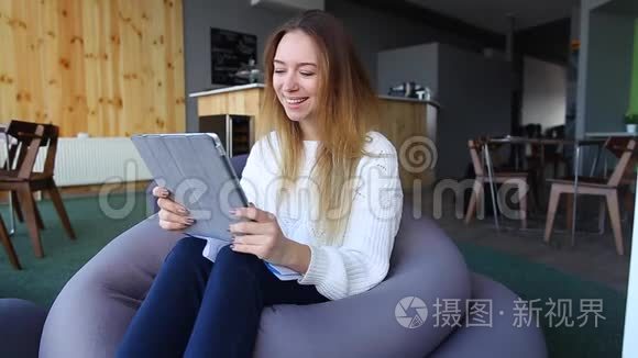 女孩手拿着平板电脑，为自己寻找有趣的信息，坐在软椅子上，在不寻常的咖啡馆里