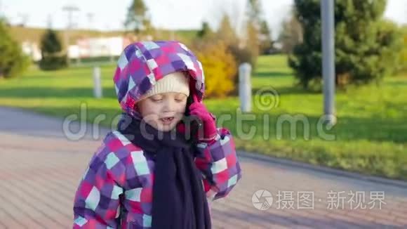 6岁女孩，穿着夹克戴着帽子在公园里打电话