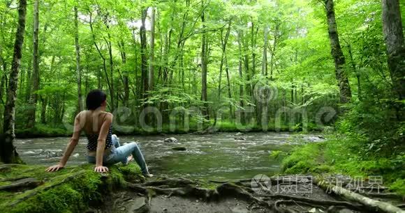 女徒步旅行者坐在深林瀑布附近。