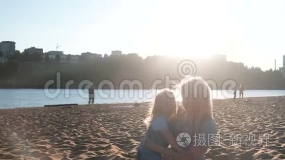 美丽快乐的金发妈妈和女儿在日落时在海滩上拥抱和说话。