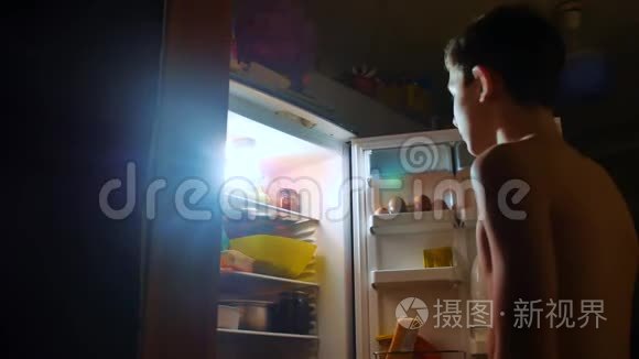 小男孩晚上从冰箱里吃饥饿和饕餮。 青少年男孩晚上看冰箱。 生活方式