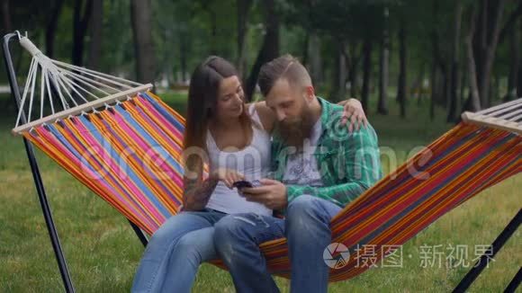 年轻夫妇带着手机坐在吊床上