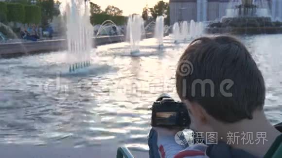 这个男孩是个十几岁的孩子，坐在喷泉旁边的一个美丽的地方，拍摄水溅的照片。 美丽的风景