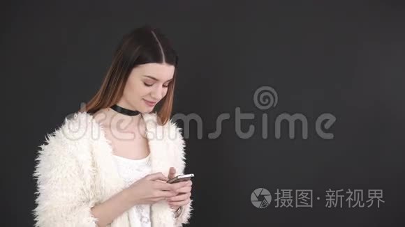 在灰色背景下使用智能手机的年轻漂亮女人。