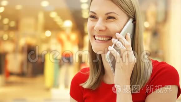 慢动作年轻女子坐在购物中心微笑。 用她的智能手机和朋友聊天