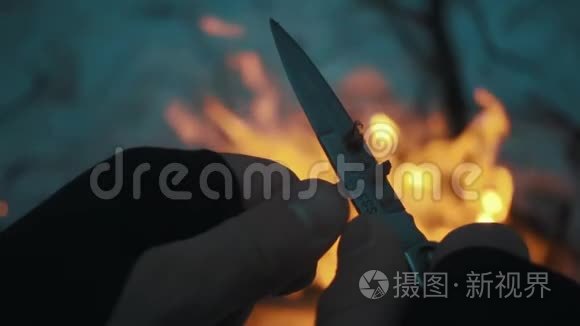 男人用刀把铅笔卷到篝火上视频