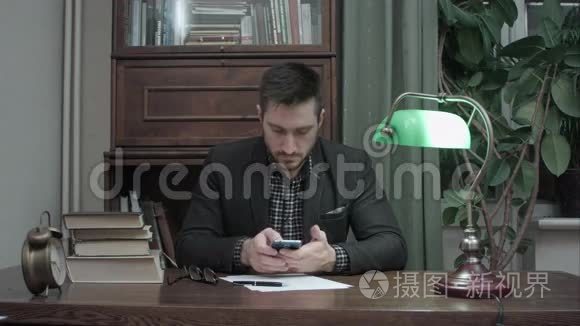 年轻人坐在书房的桌子上，拿着书，用手机