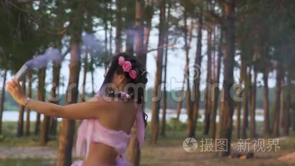 美丽的女孩，化妆鲜艳，穿着一件粉红色的连衣裙，在松树的背景上用烟雾弹跳舞。 的舞蹈
