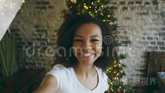 年轻的非洲裔美国女孩在家中圣诞树附近使用智能手机摄像头在线聊天
