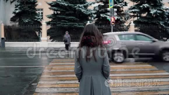 后景。 这个悲伤的年轻黑发女孩正在一个冬天白雪覆盖的城市等待绿灯过马路。