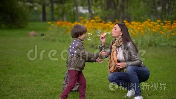 漂亮的年轻妈妈和她一个非常可爱的小儿子在夏天快乐地在户外吹泡泡。 慢动作