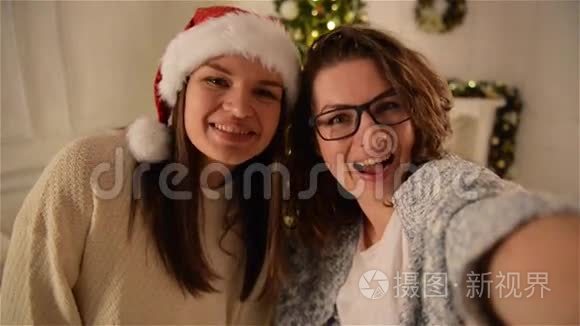 两个美丽的女孩在圣诞树背景上玩自拍。 布鲁内特修女使用智能手机