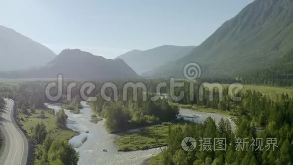 空中无人机景：在日落柔和的光线下飞越松树林、山河和乡村道路。 山区