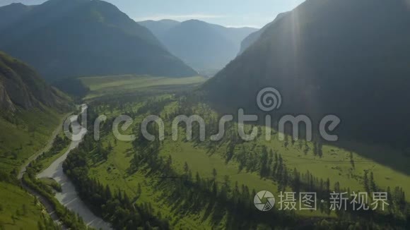 空中无人机景：在日落柔和的光线下飞越松树林、山河和乡村道路。 山区