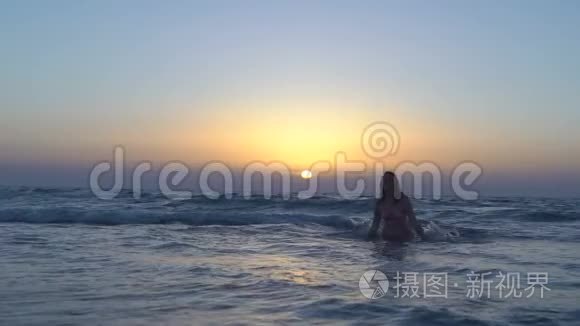 穿着粉红色泳衣的漂亮女人正在海滩上跑步晒太阳，坐在海里或海洋里。 快乐的女孩奔向日落