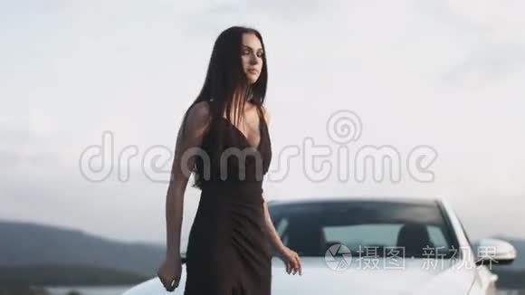 穿着黑色长裙的黑发女人站在白色汽车旁边