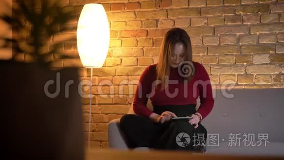 年轻漂亮的白种人女性在平板电脑上打字的特写镜头，坐在室内的沙发上