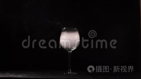 人将葡萄酒倒入带有黑色背景的液氮的玻璃杯中。