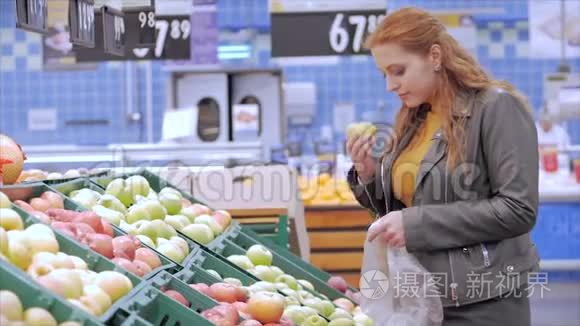 漂亮的年轻漂亮的红发女人在市场上，在超市里买食物、水果、苹果。 女孩选择产品