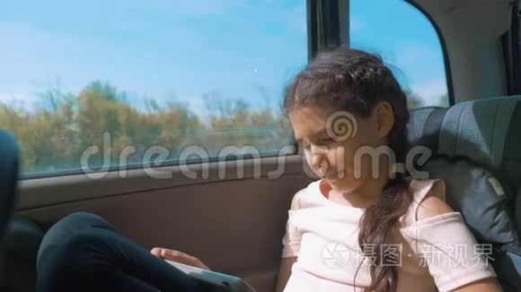 小女孩坐在车里，带着平板电脑，互联网，社交媒体去旅行。 汽车概念旅行运输女孩