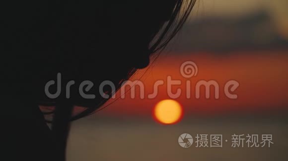 一个年轻女人坐在河边，在日落时读一本书的剪影，特写，慢动作。