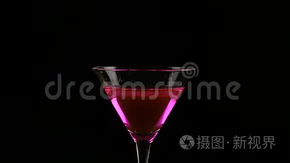 一片柠檬被扔进一个玻璃与粉红色鸡尾酒在一个黑暗的背景。 慢动作