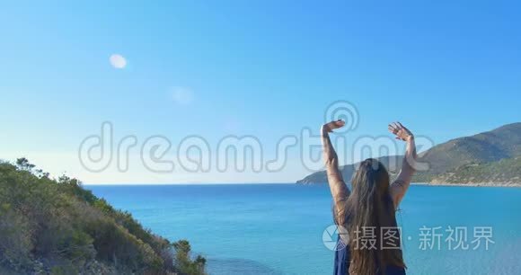 那个年轻的女孩在海上的山上举起了双手。 清澈的海水碧水..