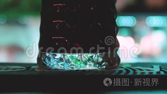 靠近酒吧柜台的彩色灯光背景与一杯饮料和酒保做他的工作。