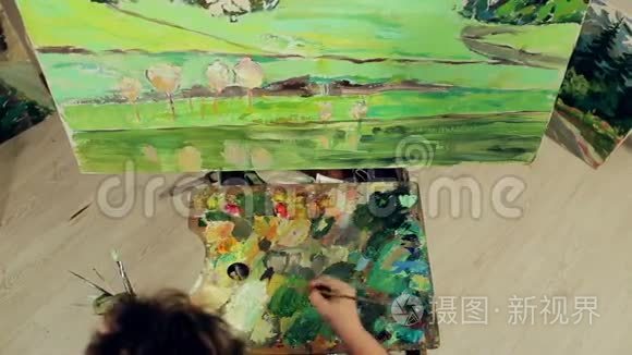 一个女人用调色板和画笔用油画颜料描绘风景。 顶部视图