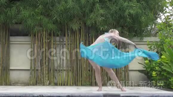 年轻苗条的女子在热带度假胜地的泳池边跳东方舞