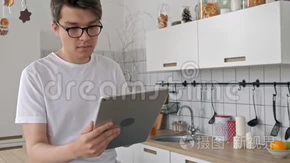 家中有魅力的男人在厨房里用平板电脑发送信息，社交媒体微笑着享受现代生活方式