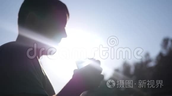 一个年轻健康的人从玻璃杯中喝干净的水，站在轮廓、光线和光线中的太阳旁边。