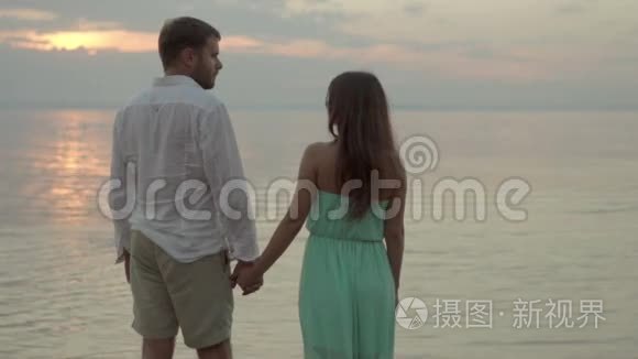 日落时分，在海滩上快乐的一对年轻夫妇牵着手互相看着