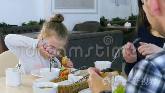 家人在餐馆吃健康的午餐。 小女儿吃白面包的蔬菜沙拉..